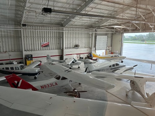 A view of several small aircraft parked inside a spacious hangar with large doors and bright lighting.