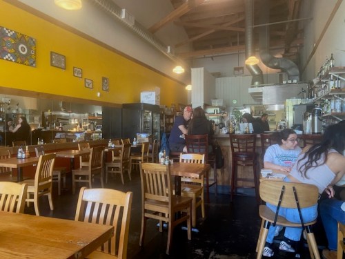 A cozy restaurant interior with wooden tables, yellow walls, and patrons enjoying their meals.