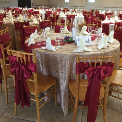 Elegant dining setup with round tables, gold chairs, and red tablecloths, ready for an event.