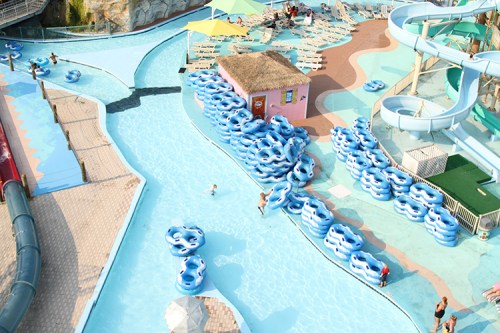 Aerial view of a water park with blue inner tubes, a lazy river, and people enjoying the sun by the poolside.