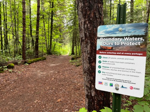 A forest path with a sign about protecting the Boundary Waters, listing guidelines for visitors before entering.