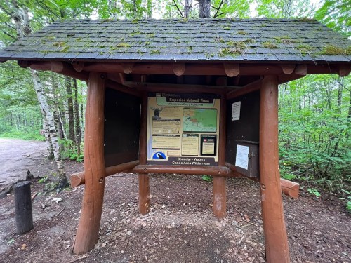 A wooden information kiosk in a forest, displaying a map and details about the Superior National Forest.