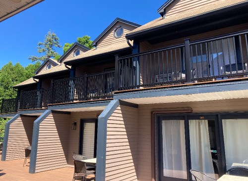 A row of two-story buildings with balconies, surrounded by trees under a clear blue sky.
