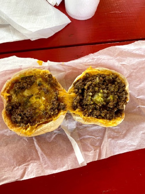 A split sandwich with melted cheese and a savory meat filling, served on a paper-lined tray.