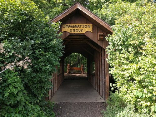 A wooden bridge entrance labeled "Imagination Grove," surrounded by lush greenery and trees.