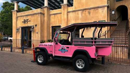 A pink jeep parked outside a building with a rustic design, featuring a sign for "Pink Jeep Tours."
