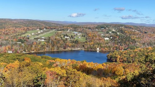 A scenic view of a lake surrounded by colorful autumn foliage and rolling hills under a clear blue sky.