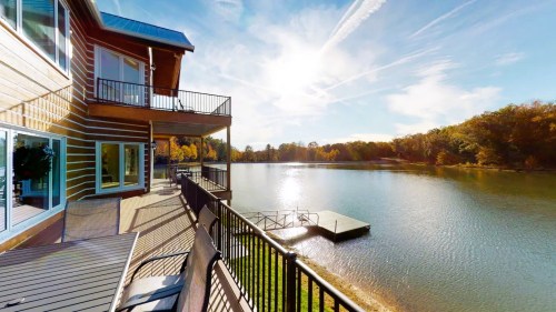 Scenic view of a lake from a balcony, with sunlight reflecting on the water and autumn trees in the background.