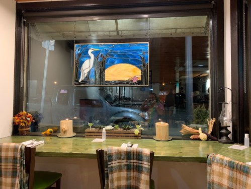 A cozy restaurant window with a painting, candles, and decorative items on a green table.