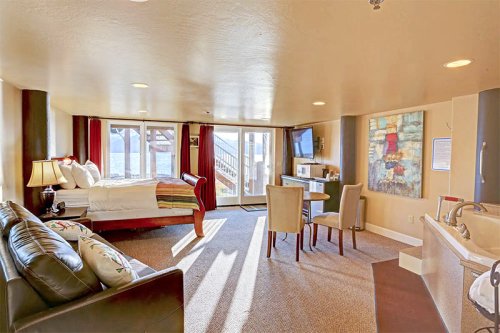 Cozy hotel room with a bed, seating area, dining table, and large windows overlooking a scenic view.