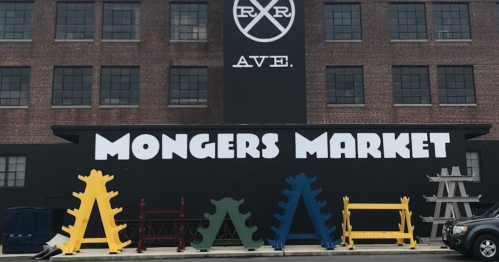 Colorful display of wooden structures in front of a building with "MONGERS MARKET" painted on the wall.