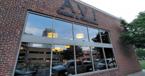 Exterior view of AVI Seabar & Chophouse, featuring large windows reflecting the city and a brick facade.