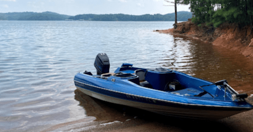 A blue boat rests on the sandy shore of a calm lake, surrounded by trees and distant hills.