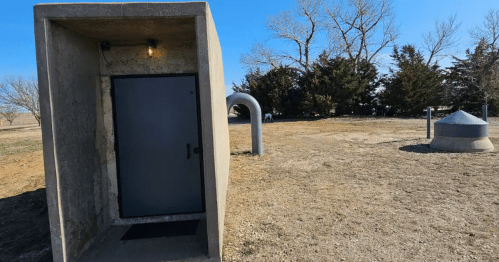 A concrete structure with a dark door, surrounded by sparse grass and trees under a clear blue sky.