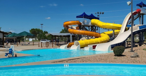 Colorful water slides next to a clear blue pool on a sunny day, with lounge areas in the background.