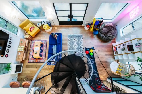 Aerial view of a modern living room with colorful furniture, a spiral staircase, and large windows.