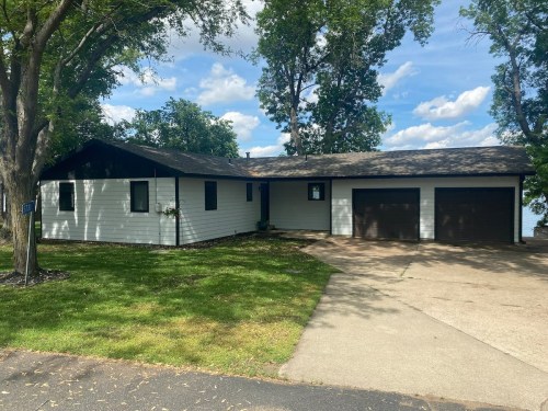 A single-story house with a black and white exterior, two garage doors, and surrounded by trees and grass.