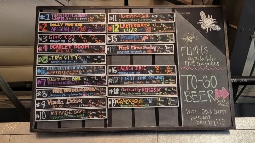 A chalkboard menu displaying various beers with names, styles, and prices, including options for flights and to-go beer.
