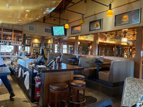 Interior of a restaurant featuring a bar, booths, and a TV, with warm lighting and a cozy atmosphere.