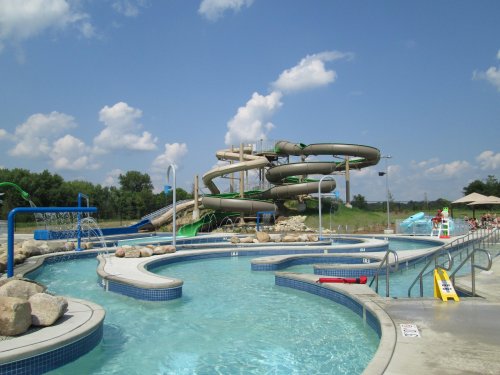 A water park featuring a large slide, pools, and splash areas under a blue sky with fluffy clouds.