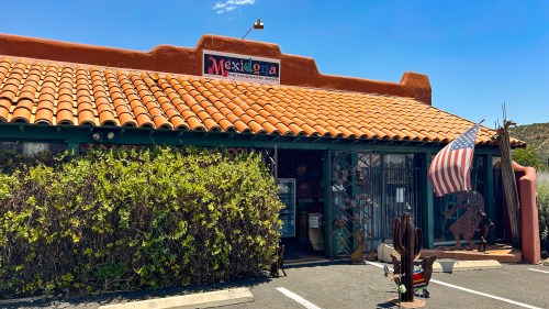 A rustic building with a tile roof, featuring a sign that reads "Mexigona" and an American flag out front.