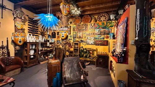 A vibrant art gallery filled with colorful masks, paintings, sculptures, and unique decor items on display.