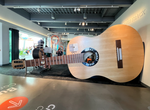 A giant acoustic guitar displayed indoors, showcasing its large body and fretboard in a modern space.