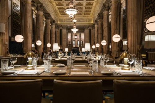 Elegant restaurant interior with ornate architecture, large columns, and tables set with glassware and cutlery.