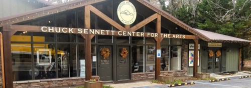 Exterior of the Chuck Sennett Center for the Arts, featuring a wooden facade and seasonal decorations.