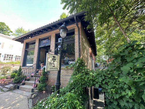 A charming brick building with a sign reading "Open," surrounded by greenery and a lamp post.