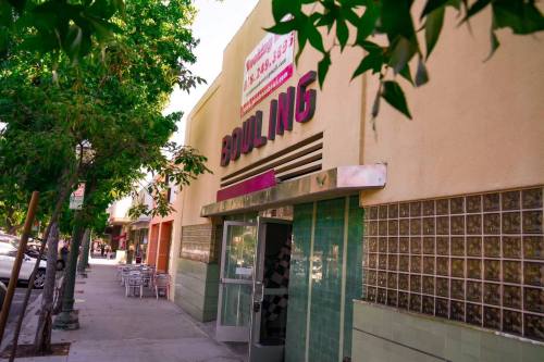 A bowling alley with a bright sign, surrounded by trees and outdoor seating, on a sunny day.