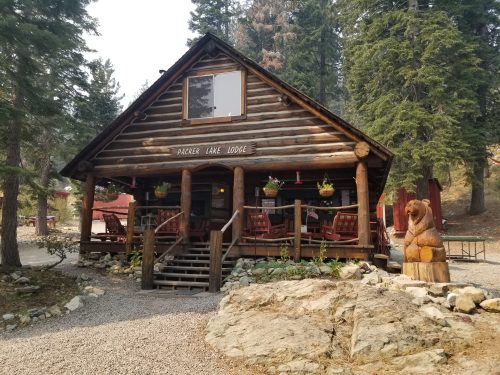 A rustic log cabin with a porch, surrounded by trees and a bear sculpture, at Parker Lake Lodge.