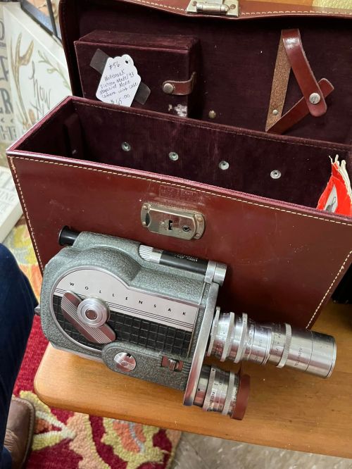 A vintage Wollensak movie camera in a brown case, resting on a table with a patterned surface.
