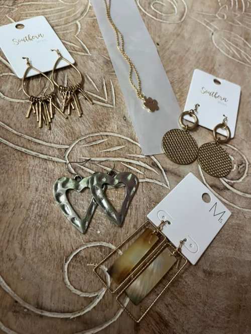 A collection of various earrings and a necklace displayed on a wooden surface, each with tags.