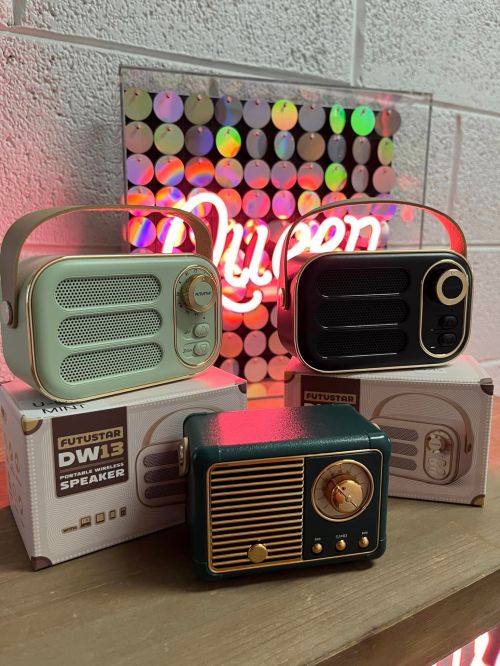 Three vintage-style speakers displayed on a shelf, with a colorful "Queen" sign in the background.