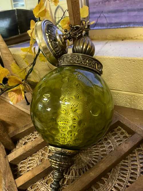 A decorative green glass lantern with intricate lace patterns, resting on a wooden surface with autumn leaves.