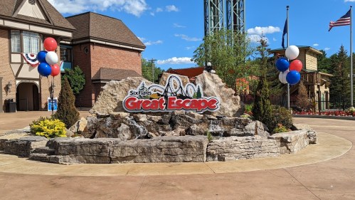 Entrance sign for Six Flags Great Escape, featuring a rock formation and colorful balloons in a sunny outdoor setting.