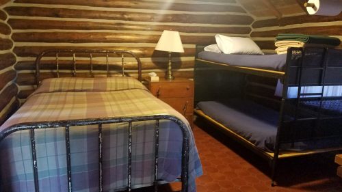 Cozy cabin interior featuring a single bed, bunk bed, lamp, and wooden walls.