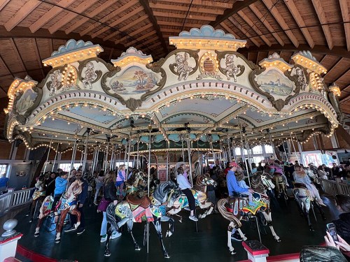 A colorful carousel with ornate decorations and riders on horses, set in a spacious indoor area.