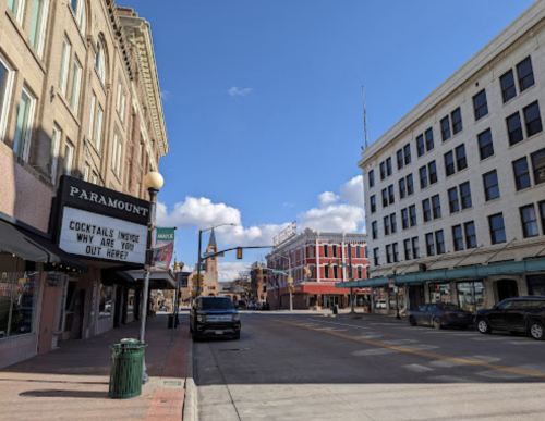 A street view featuring buildings with signs, a clear blue sky, and a parked car on a sunny day.