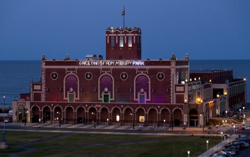 Historic building at Asbury Park, illuminated at dusk with "Greetings from Asbury Park" sign and ocean in the background.