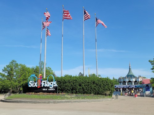 Entrance to Six Flags Great America, featuring flags and a welcoming sign against a clear blue sky.
