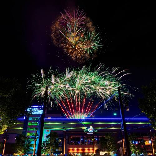 Colorful fireworks burst in the night sky above a brightly lit building, creating a festive atmosphere.
