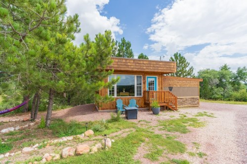 A cozy wooden cabin surrounded by trees, featuring a porch with chairs and a gravel pathway.