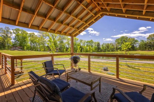A cozy deck with seating and a grill, overlooking a green landscape and pond under a clear blue sky.