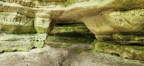 A rocky cave interior with greenish hues and ancient carvings on the walls, showcasing natural textures and formations.