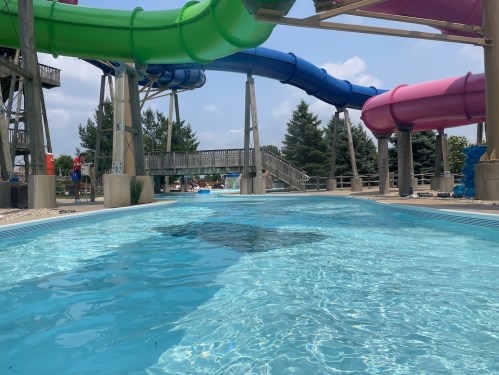 Colorful water slides above a clear pool, with trees and people in the background on a sunny day.