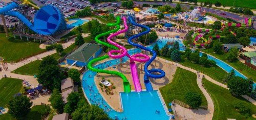 Aerial view of a vibrant water park featuring colorful slides, pools, and lush green areas with visitors enjoying the attractions.