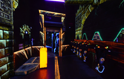 A dimly lit room with neon accents, featuring stone walls and a glowing yellow object near a row of equipment.