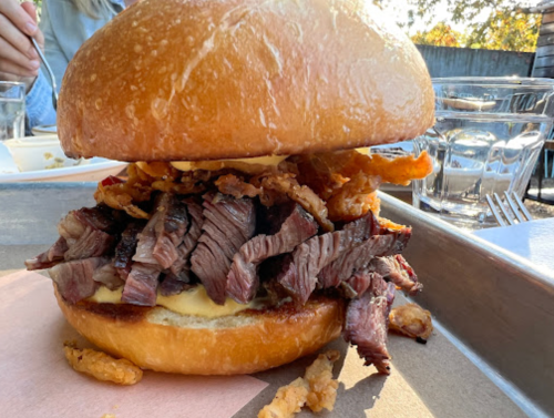 A large sandwich filled with sliced beef, crispy onions, and melted cheese, served on a toasted bun.
